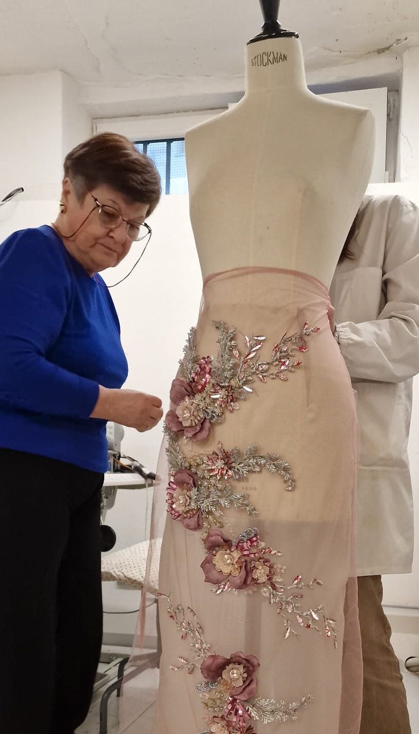 A seamstress beside a mannequin wearing a skirt embroidered with flowers